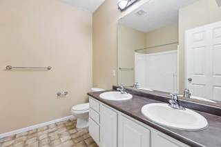 Apartment bathroom with double-sink vanity, large mirror, white cabinetry, and tub shower combo.