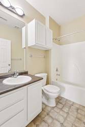 Apartment bathroom with white vanity, large mirror, tub shower combo, and patterned tile flooring.