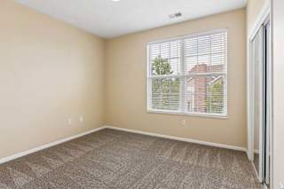 Bright apartment bedroom with large window, beige walls, carpet, and mirrored closet doors.