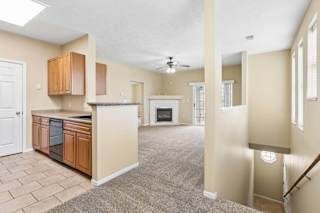 Open apartment interior with kitchen, carpeted living room, fireplace, windows, and stairway landing.