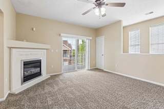 Carpeted apartment living room with fireplace, ceiling fan, sliding glass doors, and private balcony access.