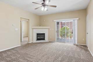 Apartment living room with carpet, fireplace, ceiling fan, and sliding glass doors leading to a balcony.