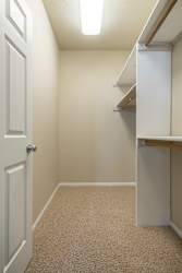 A white door is on the left of a hallway with a carpeted floor.