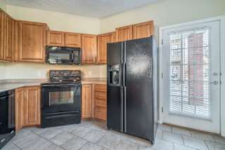 A black refrigerator stands in a kitchen with wooden cabinets and a black microwave.