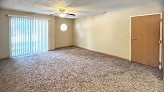 a living room with a ceiling fan, carpeted floor, a sliding glass door with vertical blinds