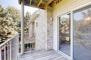 Private apartment balcony with sliding glass door, brick exterior, wood ceiling, and views of surrounding trees and neighboring buildings.