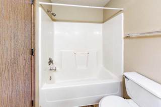 Full bathroom with white tub and shower surround, chrome fixtures, and adjacent toilet in a neutral interior.