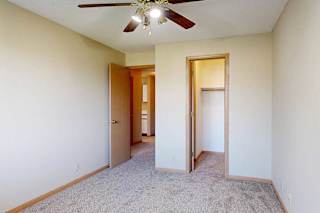 Carpeted bedroom with ceiling fan, open closet, and wood-trim doors leading to hallway and closet.
