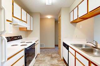 Galley kitchen with white appliances, electric stove, range hood, and wood-trim cabinetry.