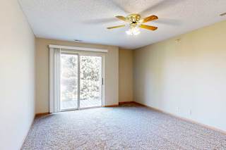 Spacious living room with sliding glass door to balcony, neutral walls, and ceiling fan with light.
