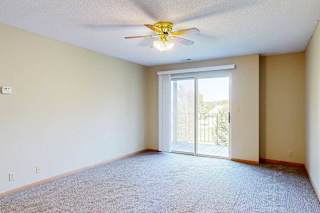 Carpeted living area with large sliding glass door, vertical blinds, and access to private balcony.