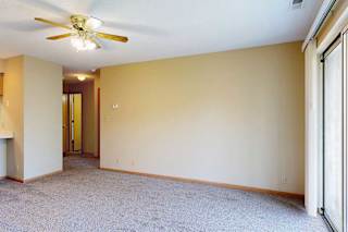 Open living room with beige walls, ceiling fan, and view toward kitchen and hallway.