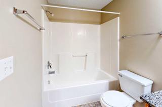 Apartment bathroom featuring a full-size tub and shower combo, neutral walls, toilet, and towel bars