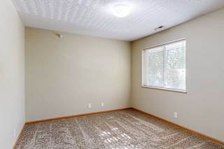 Bright bedroom with beige walls, plush carpet, wood trim, and a large window with blinds bringing in natural light.