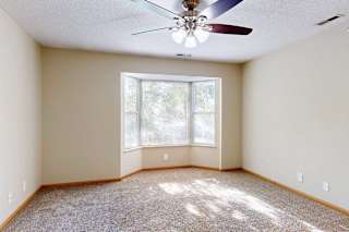 Spacious living room with plush carpet, ceiling fan with light, and bay window bringing in natural light.
