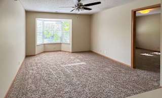 a carpeted living room with a ceiling fan and a large bay-style window