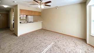 a carpeted living room with a ceiling fan, and a kitchen with a windowed countertop for dining seating
