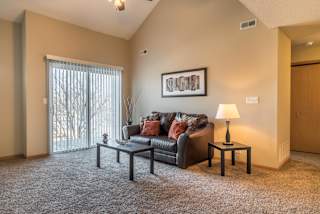 A living room with a grey couch, a small table with a lamp, and a framed picture on the wall.