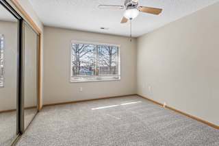 Carpeted bedroom with ceiling fan, window, and mirrored closet doors.