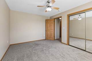 Carpeted bedroom with ceiling fan, mirrored closet doors, and interior doorway.
