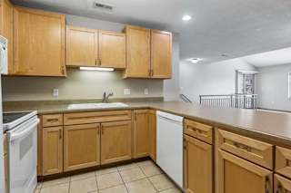 Apartment kitchen with wood cabinetry, laminate countertops, and white dishwasher.