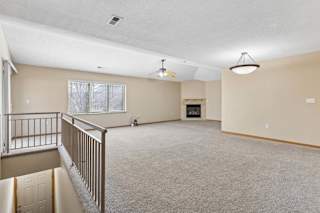 Spacious upper-level living area with carpeted floors, railing overlook, and fireplace.