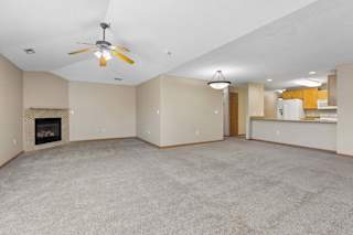 Carpeted living room with fireplace, ceiling fan, and kitchen view.