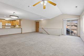 Open upper-level living area with carpeted floors, ceiling fan, railing overlook, and balcony access.