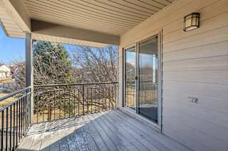 Covered apartment balcony with wood decking, metal railing, and sliding glass door.