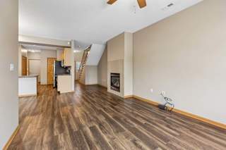 Open living room with wood-style flooring, gas fireplace, staircase, and adjacent kitchen.