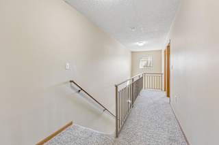 Upper-level apartment hallway with neutral carpet, stair railing, and natural light from a distant window.