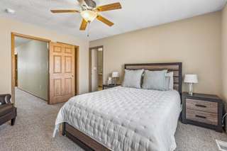 A bedroom with a large bed, a ceiling fan, and a nightstand with a lamp.