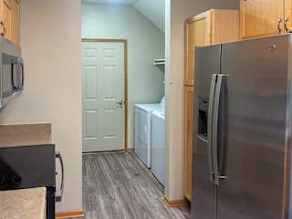 a kitchen with wooden cabinets and stainless steel appliances, with a laundry room in the background