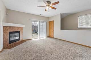 Bright apartment living room with beige carpet, tiled fireplace, ceiling fan, and sliding glass doors leading to a balcony.