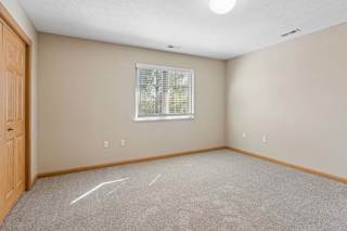 Bright, empty bedroom with neutral carpet, a large window with blinds, wood trim, and double closet doors.