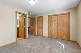 Empty bedroom with neutral carpet, double closet doors, wood trim, overhead lighting, and direct bathroom access.