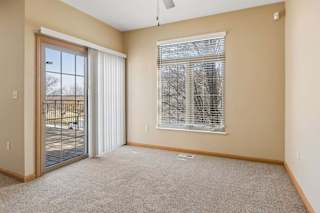 Bright, empty living area with neutral carpet, large window with blinds, ceiling fan, and sliding glass door to the deck.