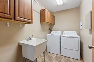 Laundry room with washer and dryer, utility sink, wood storage cabinets, tile flooring, and overhead lighting.