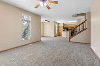 Spacious, empty living area with neutral carpet, ceiling fans, tall windows, open kitchen, and wood-railed staircase.