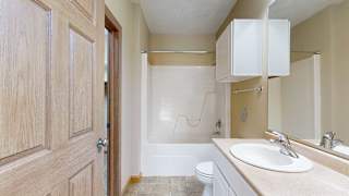a bathroom with a vanity sink, a toilet, overhead storage, and a shower tub