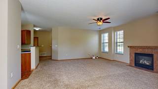 a living room with a fireplace and a ceiling fan adjacent to a kitchen