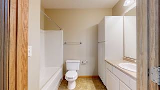 a bathroom with a toilet, a sink, a shower tub, and tall white storage cabinets