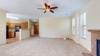 a living room with a ceiling fan next to a kitchen