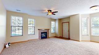 a living room with a fireplace, a ceiling fan, several tall windows, and a front door