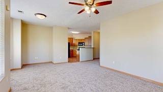 a living room with a ceiling fan next to a kitchen countertop