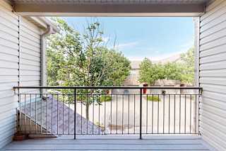 A balcony with a black railing and a view of landscaping and surrounding apartments.