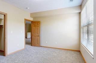 A carpeted bedroom with a large window from plenty of natural light, and an open door to the living room.