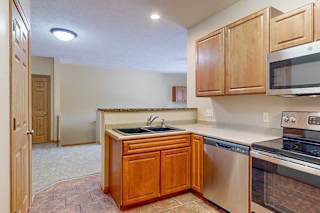 A kitchen with a double basin stone sink, wooden cabinets, and stainless steel appliances.