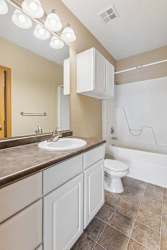 Apartment bathroom with a white vanity, large wall mirror, overhead lighting, tile flooring, and a tub-shower combination.