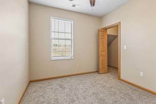Cozy apartment bedroom with neutral carpeting, a tall window with blinds, ceiling fan, and wood-trimmed doorway.